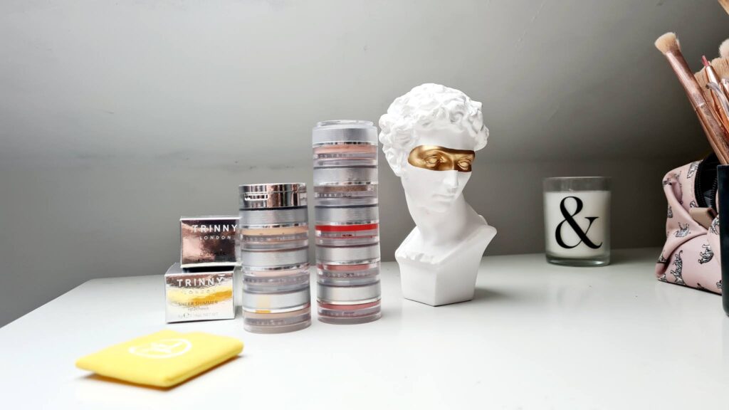 Trinny London makeup stack on a dressing table with a decorative Roman bust