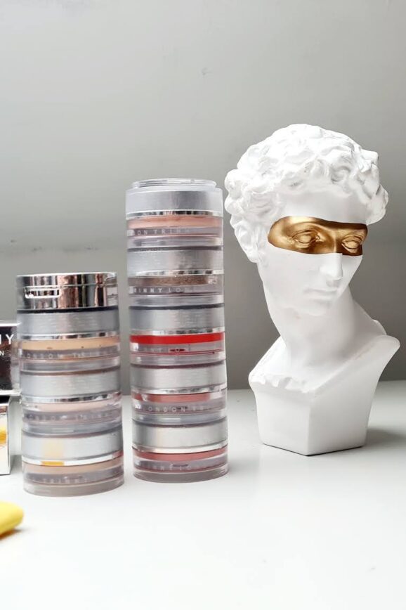 Trinny London makeup stack on a dressing table with a decorative Roman bust