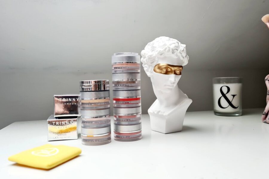 Trinny London makeup stack on a dressing table with a decorative Roman bust