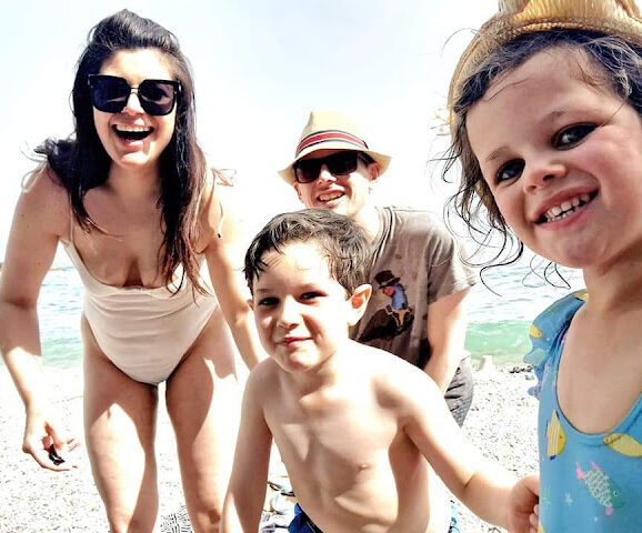 Smiling happy family on an Italian beach, mother in a white swimsuit, father at the back in a straw fedora, a little boy in swimming trunks and a little girl in a sunhat