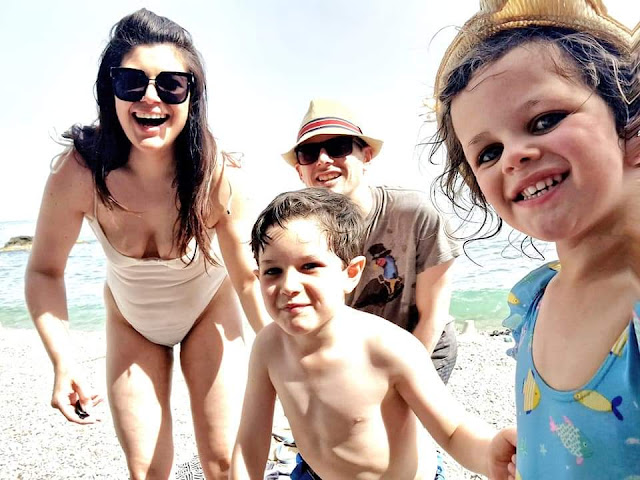 Smiling happy family on an Italian beach, mother in a white swimsuit, father at the back in a straw fedora, a little boy in swimming trunks and a little girl in a sunhat