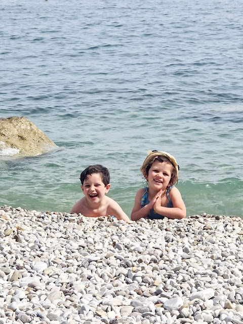 Two small children, a boy and a girl, smiling into the camera as they play in the waves.
