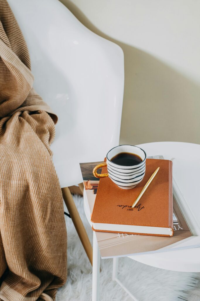 A calm scene of a cup of coffee in a handmade mug balanced on top of a pile of books 
